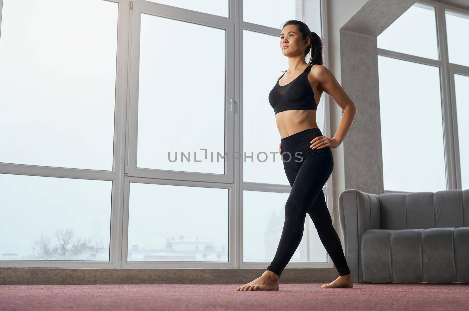 Side view of caucasian woman staying in position of yoga, looking straight while training at home. Slim female yogi with ponytail practicing yoga exercise in spacious studio. Concept of yoga practice.