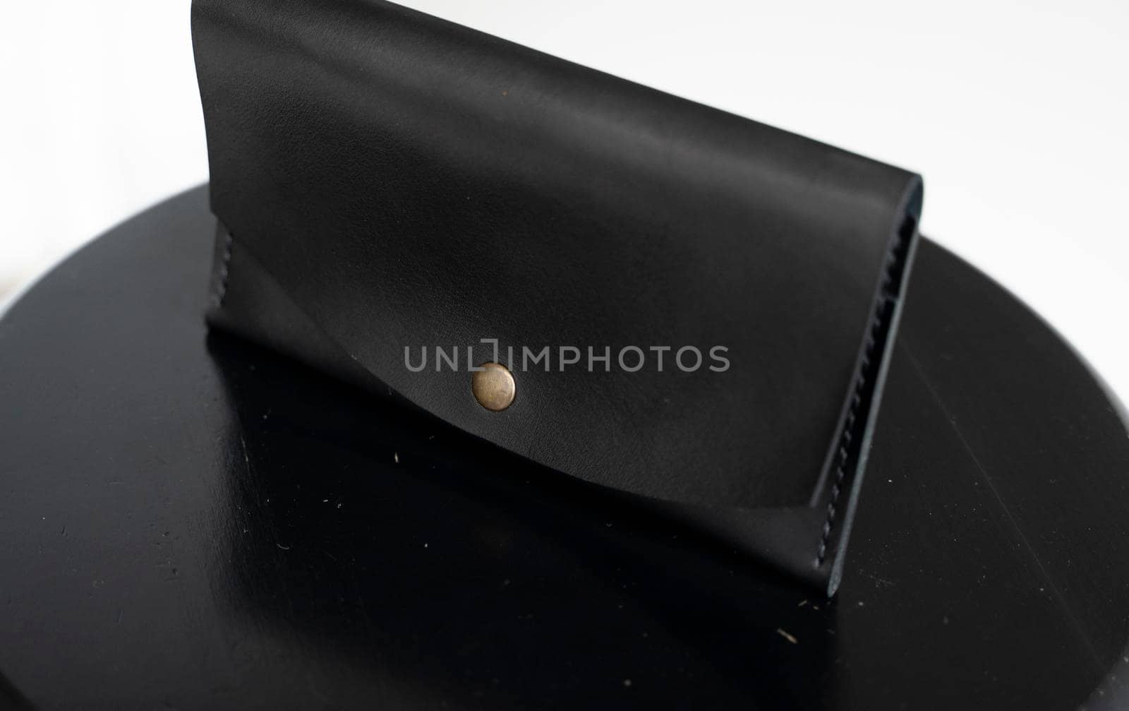 Man's handmade genuine leather wallet for banknotes and credit cards on a black surface with white background. Style, retro, fashion, vintage and elegance