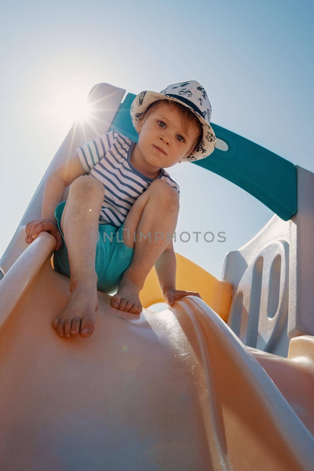 The little boy in a sunny day at the top of the slider he not dare to slip down. by Lincikas