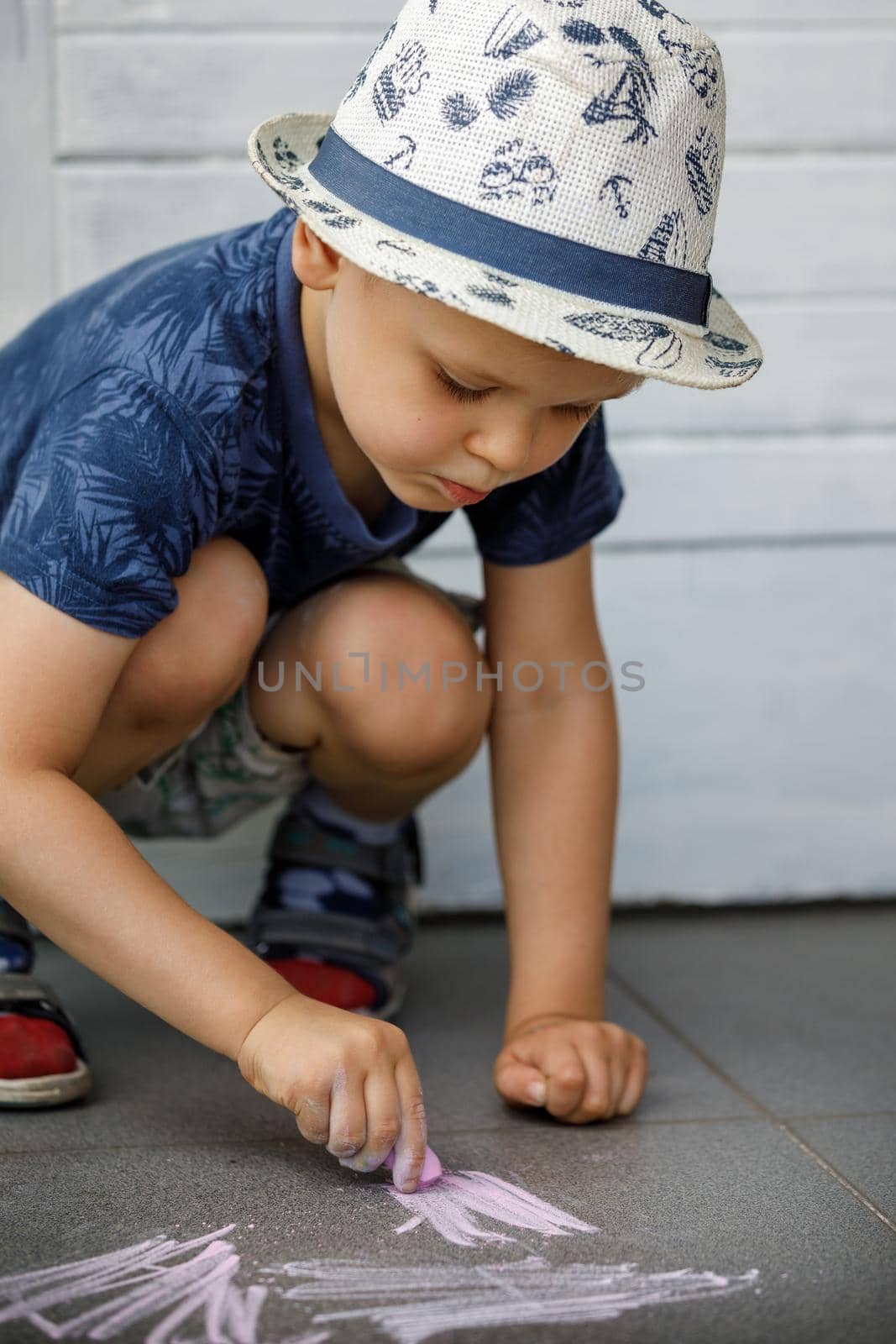 A boy draws with crayons on the asphalt . Painting. Summer games on the street. Childrens entertainment and leisure. Child puts a lot of effort and learns.