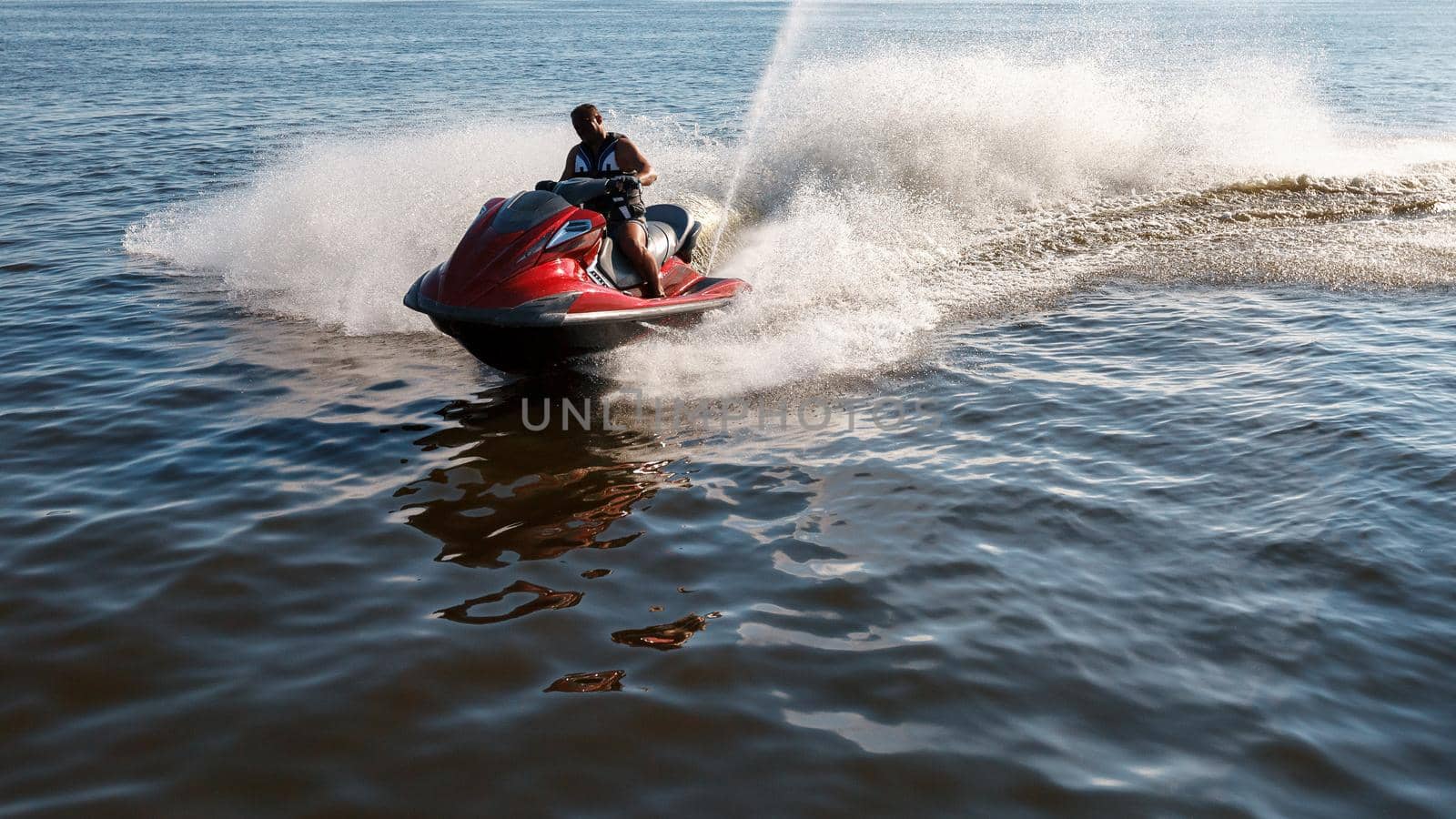 Man drives red jet ski on turquoise sea on a blue day. by Lincikas