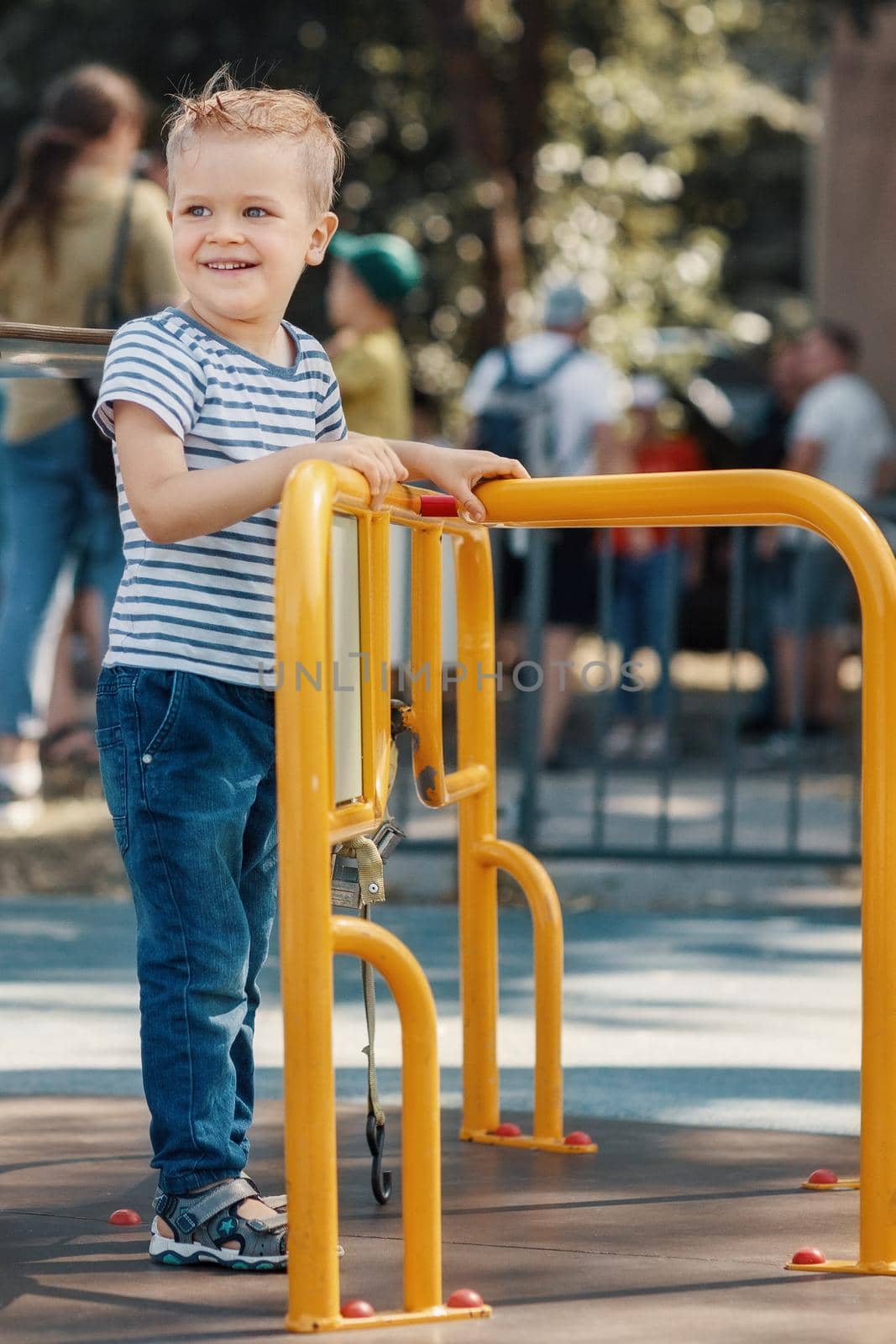 A little smiling boy in a playground on a yellow carousel. by Lincikas