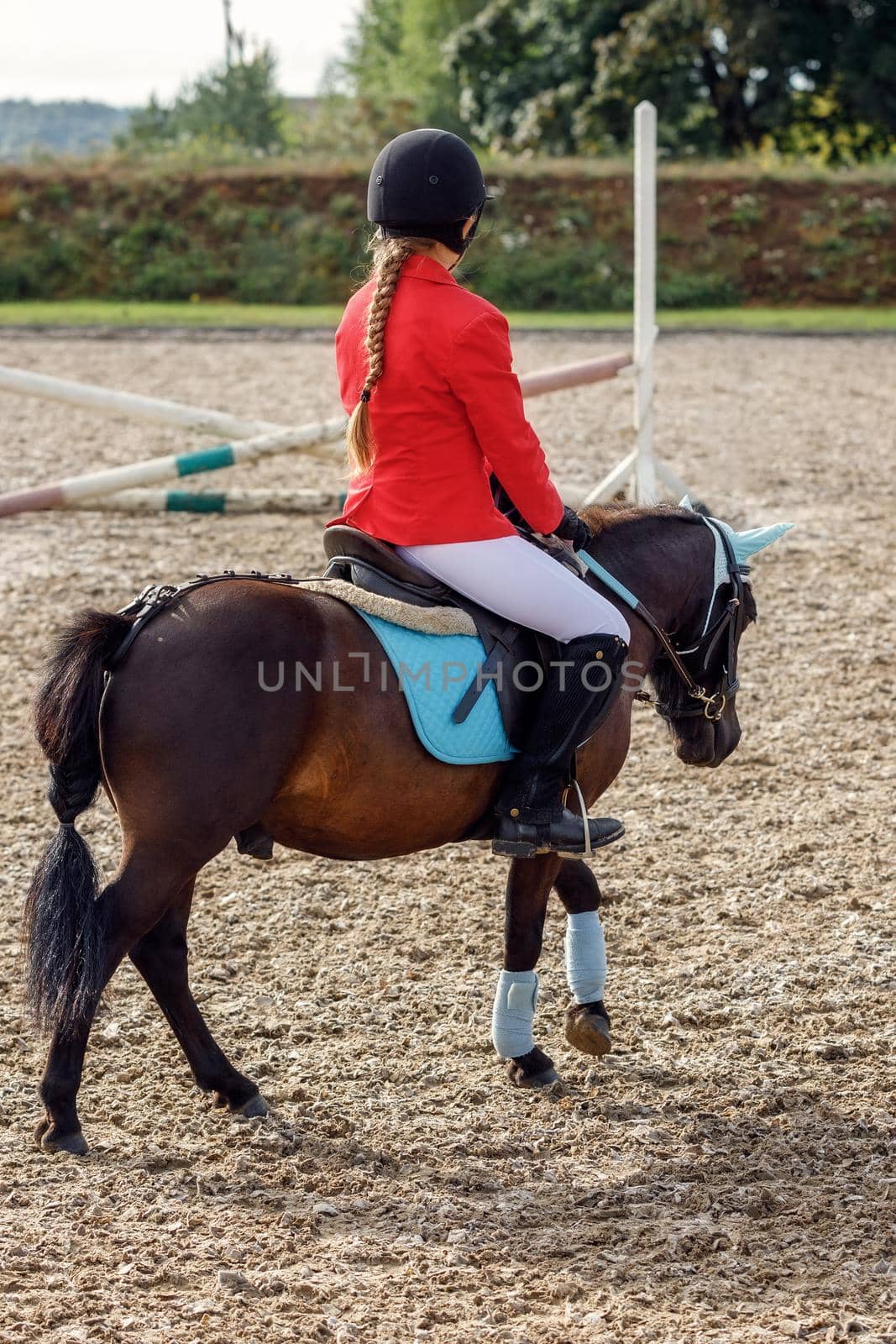 Girl in red riding clothing riding on pony over small jumps by Lincikas