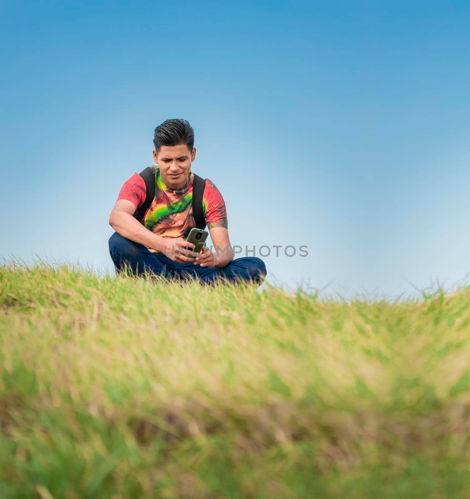 backpacker with phone on top of a hill , a man sitting on the grass with his cell phone