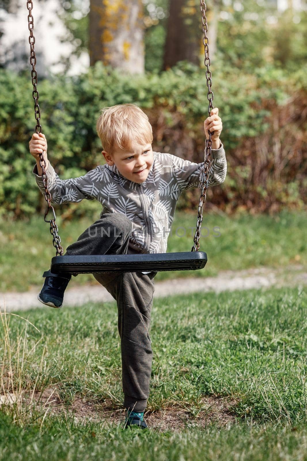 The blond boy plays with a chain swing as he tries to climb on it without his parents help.