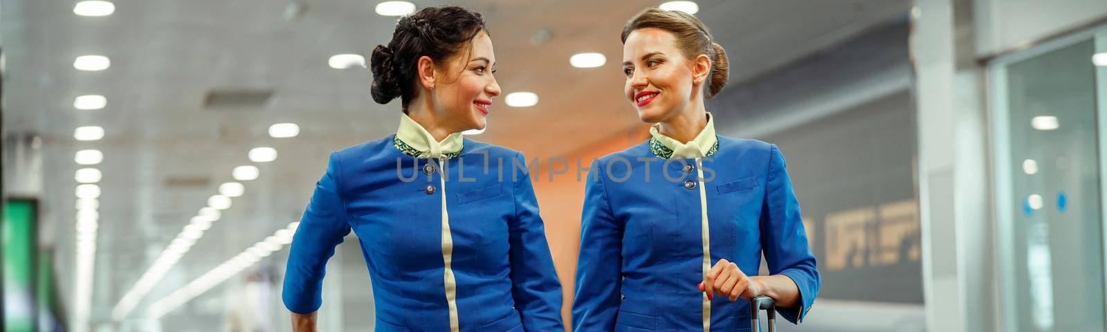 Joyful female flight attendants in air hostess uniform looking at each other and smiling while waiting for airplane