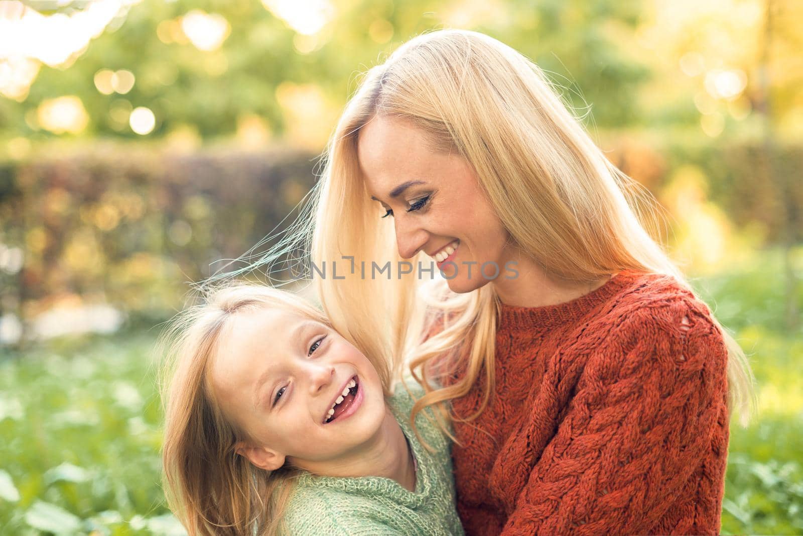Beautiful young caucasian mother and little daughter smiling together on the green grass in the Autumn Park