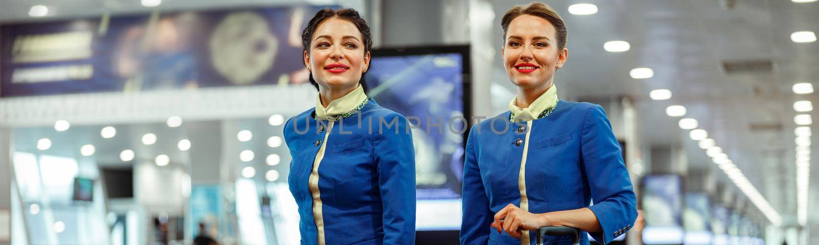 Smiling female flight attendants in aviation air hostess uniform carrying travel bags at airport