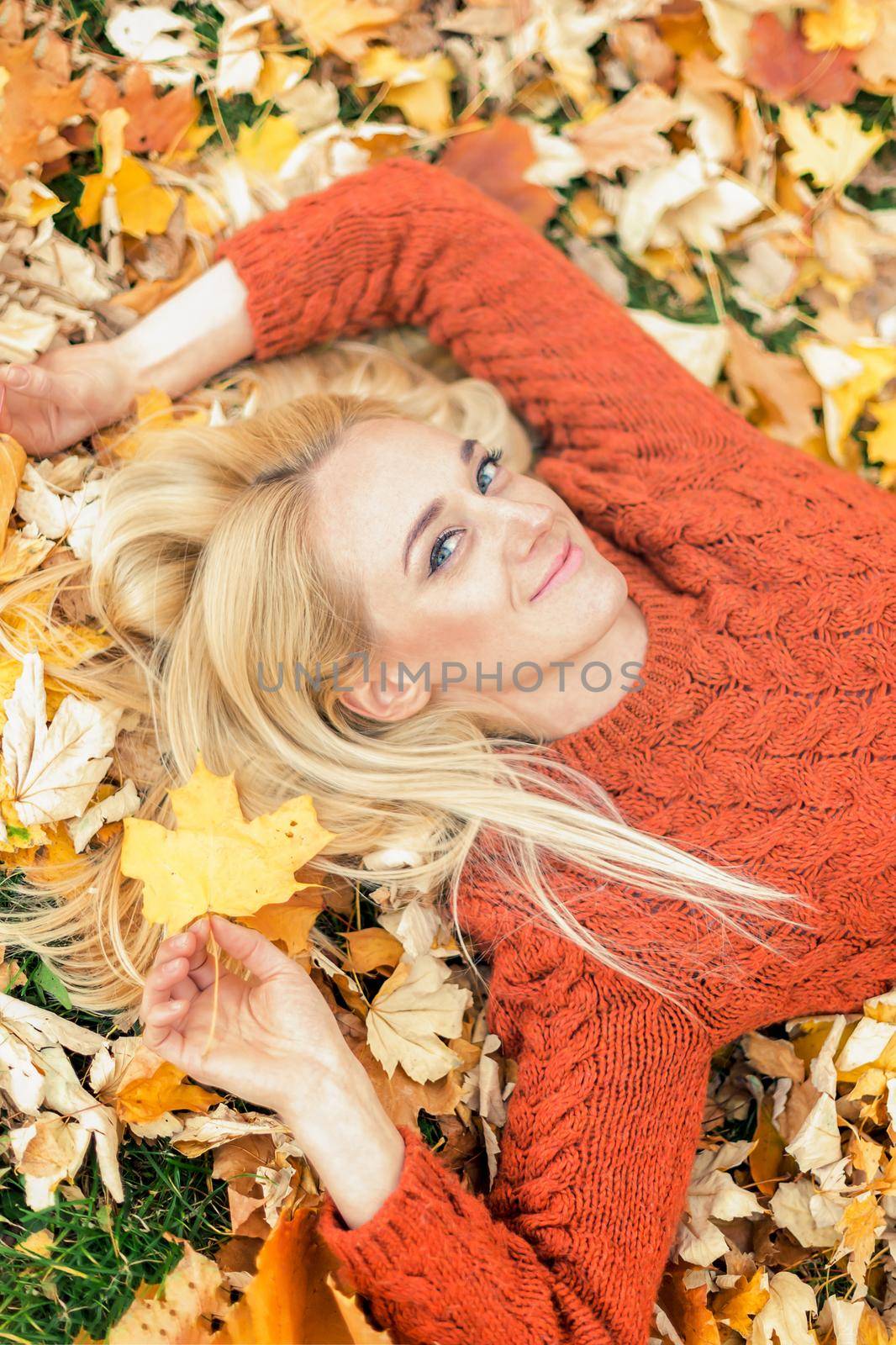 Beautiful young caucasian woman lying down on yellow leaves looking at camera in Autumn Park