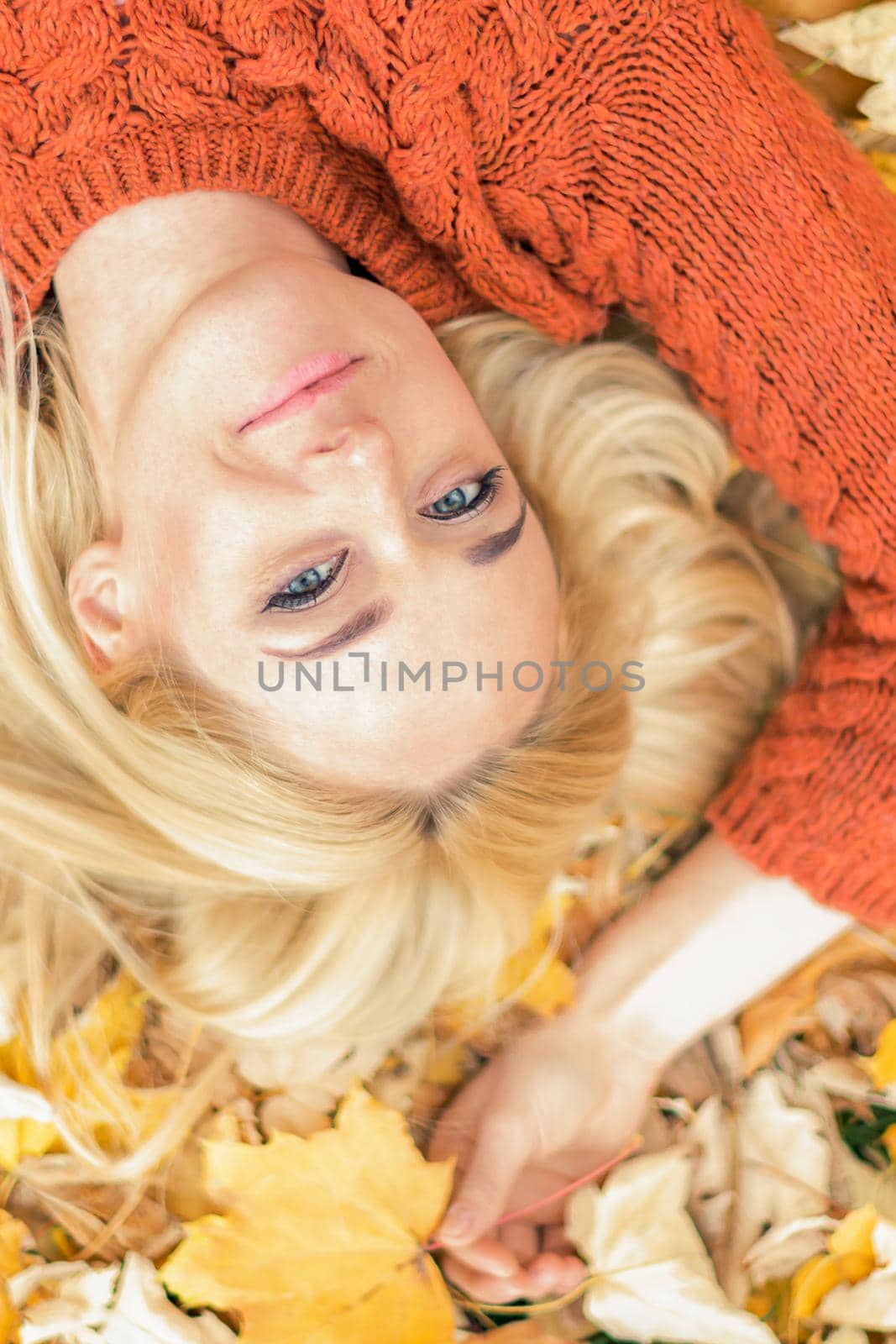 Beautiful young caucasian woman lying down on yellow leaves looking at camera in Autumn Park