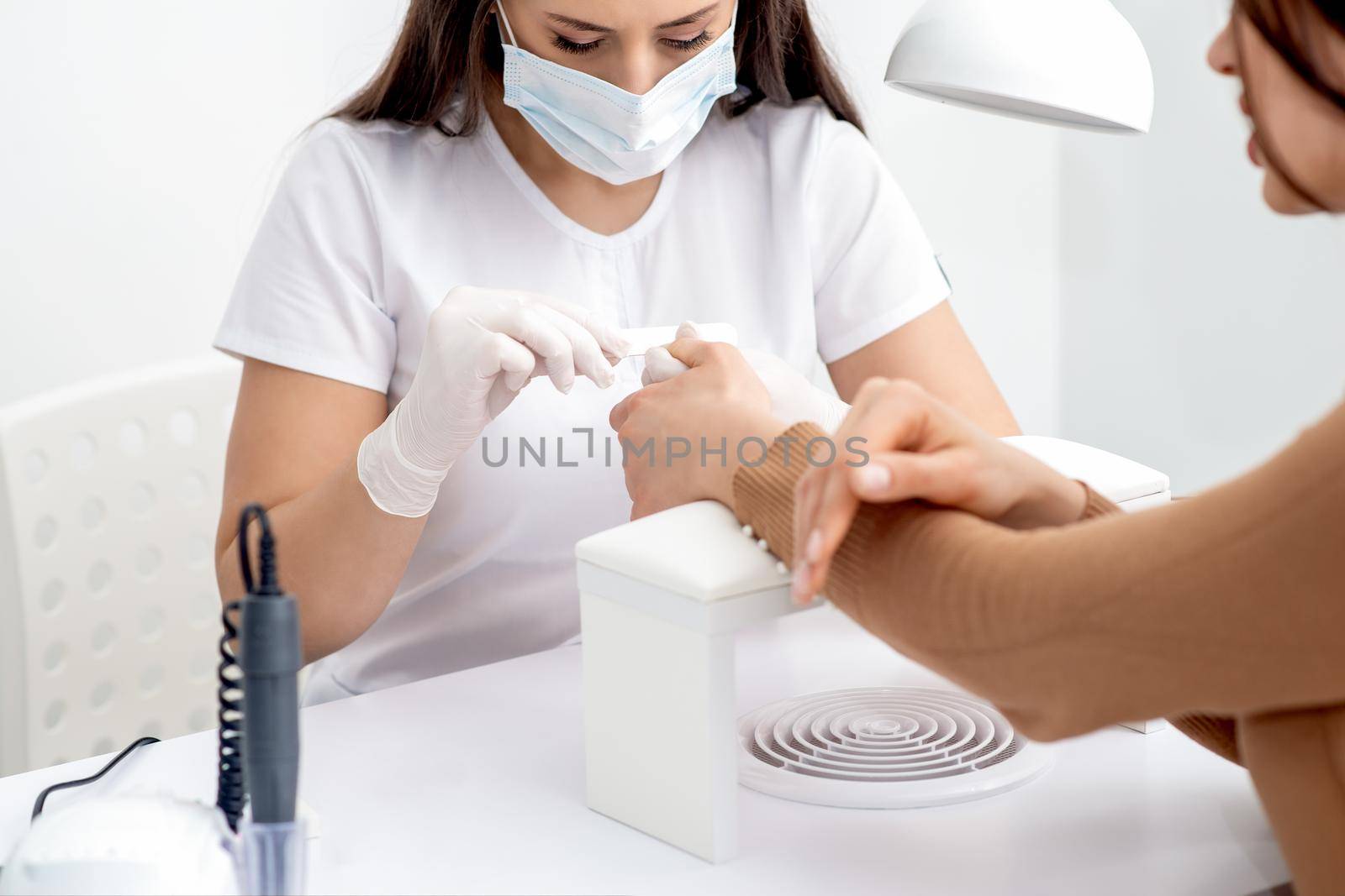 Young woman receiving a manicure by a beautician with nail file in a nail salon. Manicurist filing client's nails