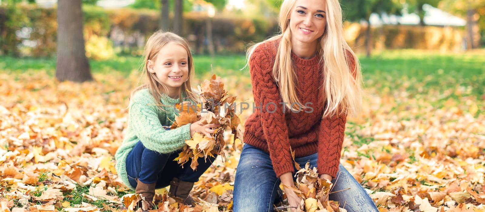 Happy young caucasian mother and little child playing with leaves in nature autumn park