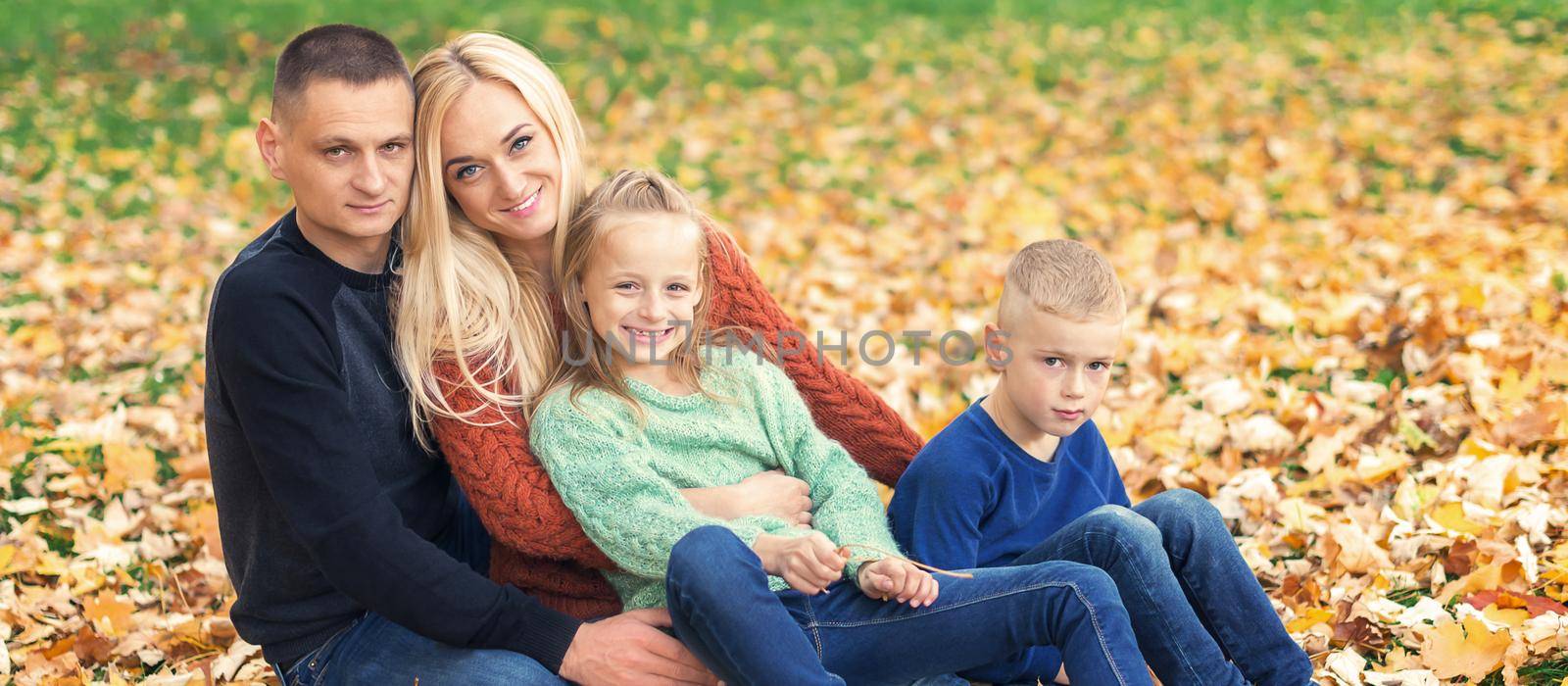 Portrait of young family sitting in autumn leaves by okskukuruza