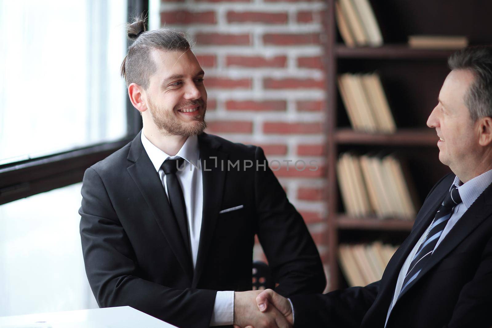 friendly handshake of business partners sitting at a Desk by SmartPhotoLab