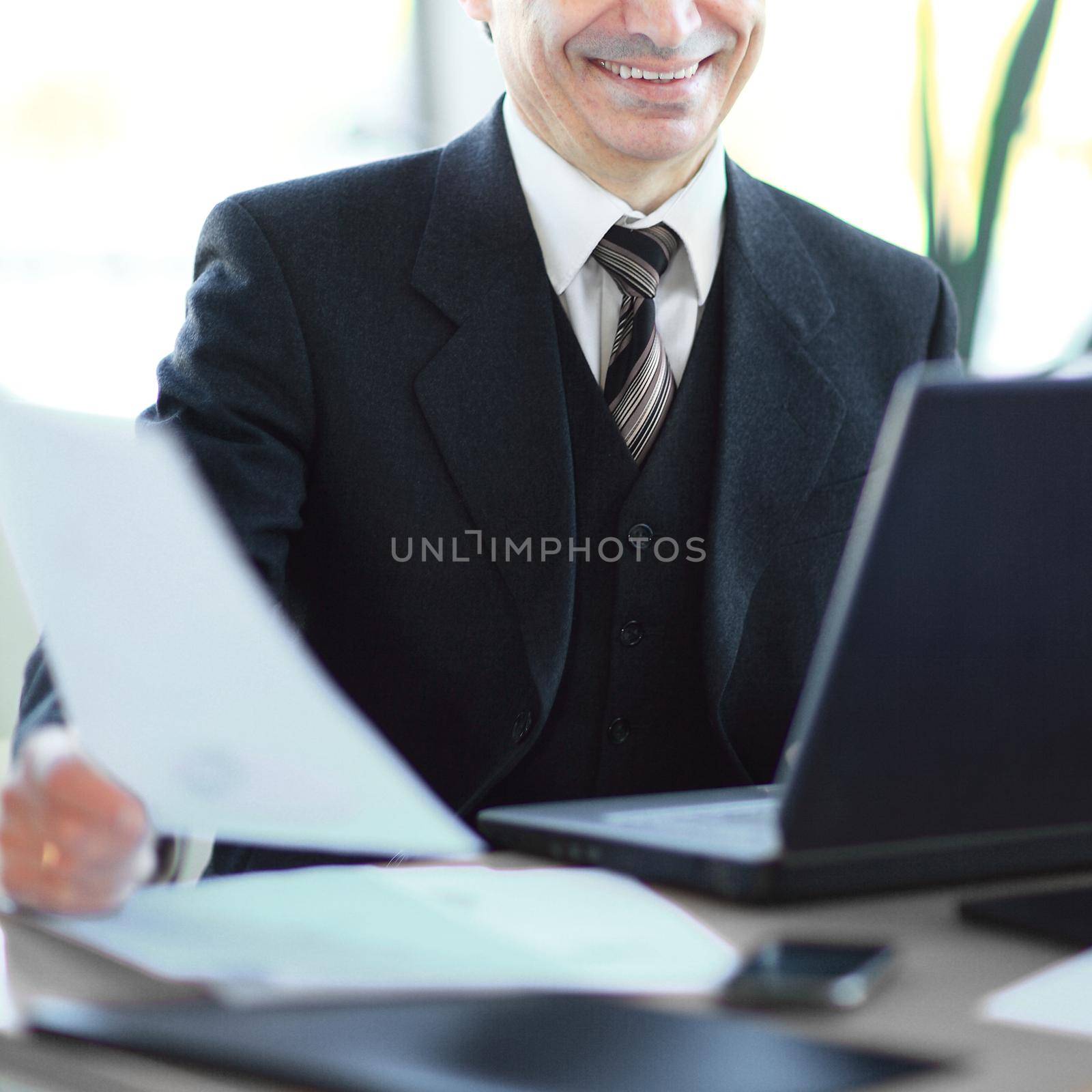 smiling senior businessman sitting at his Desk. business concept. by SmartPhotoLab