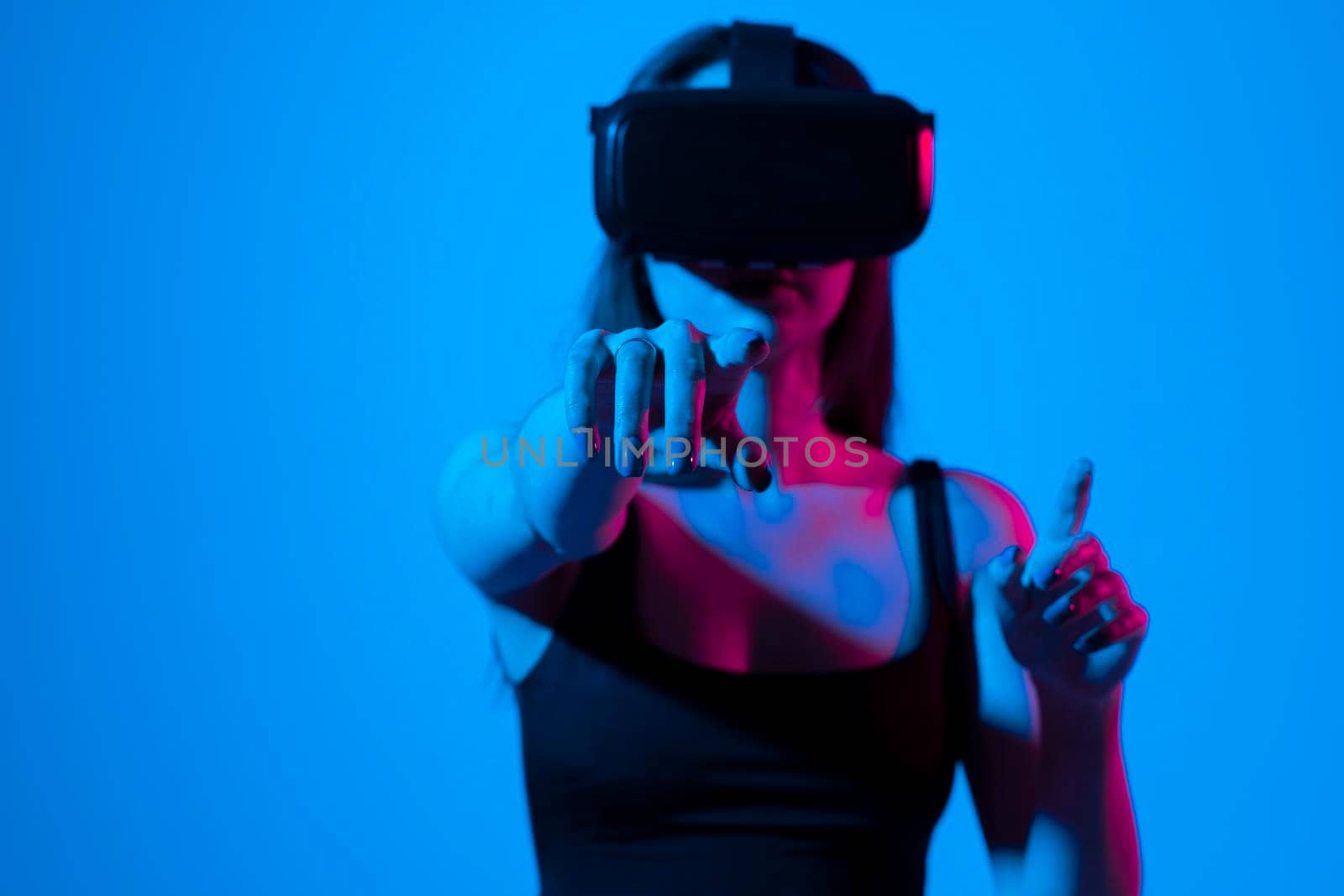 Young woman wearing VR goggles and interacts with cyberspace using swipe and stretching gestures while playing a video game with a friends in metaverse. by vovsht