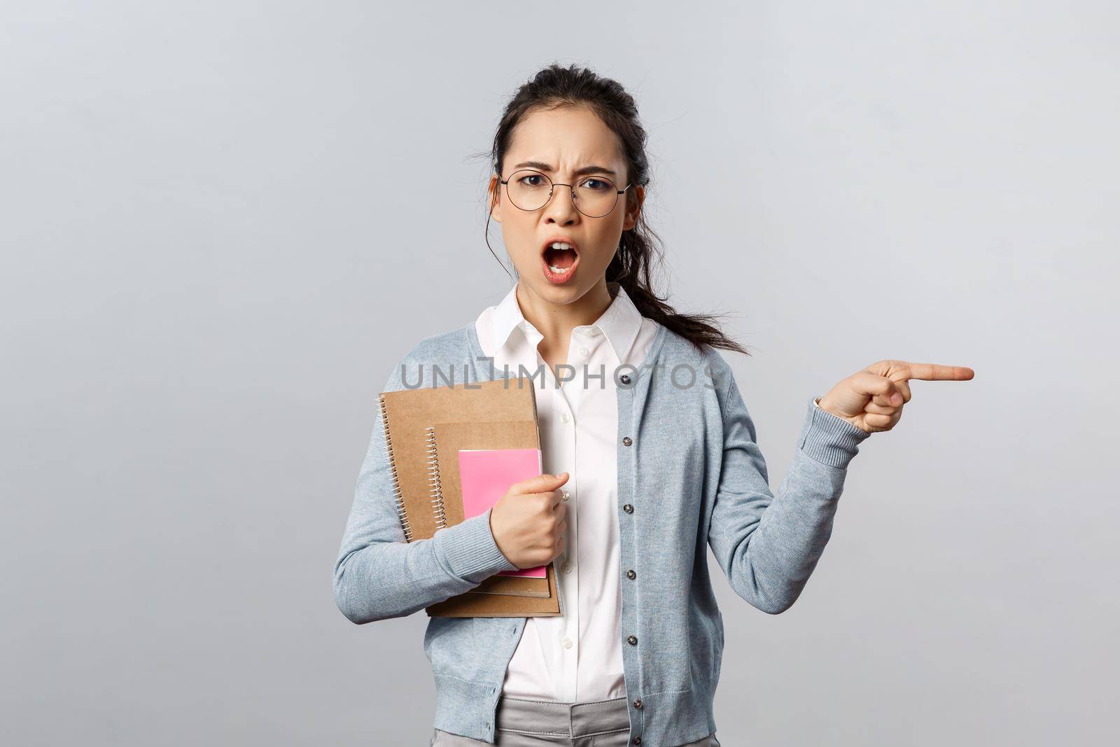 Education, teachers, university and schools concept. Angry and displeased strict tutor, teacher scolding student and tell leave class now, pointing at door shouting annoyed, grey background.