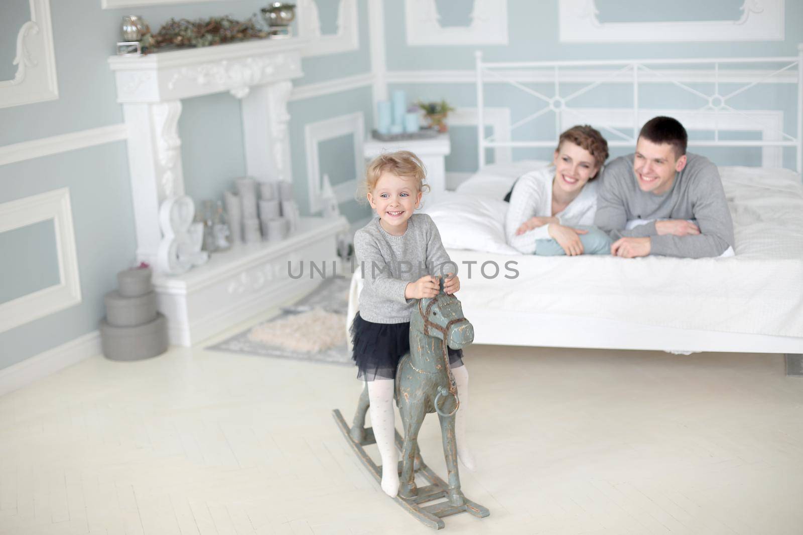 Happy family of three sit in room and play with daughter on her wooden toy horse.family happiness