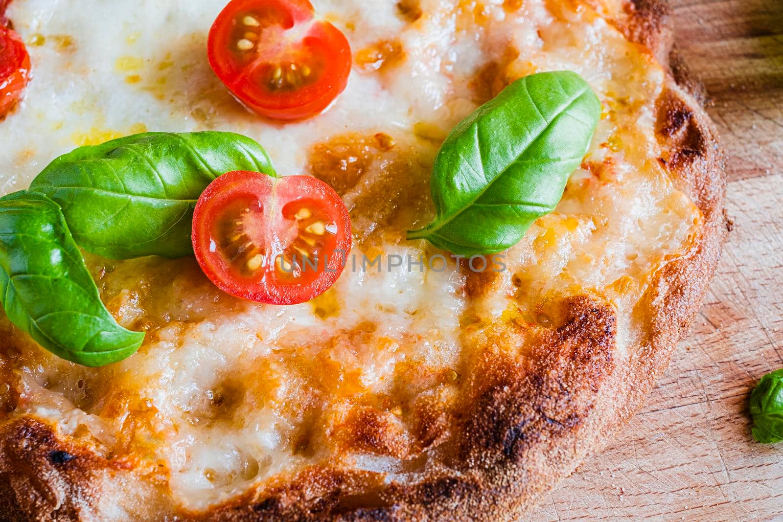 vegetarian pizza with addition of cheese, fresh tomatoes, basil on a wooden rustic table.