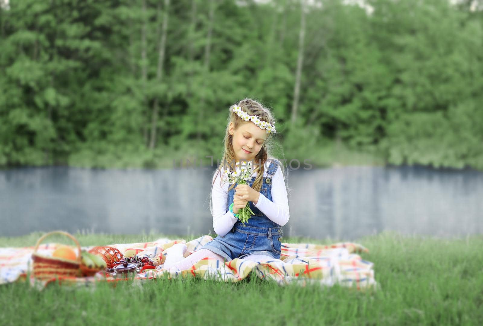 cute little girl in a wreath and a bouquet of wildflowers on a picnic in the woods on a Sunny day