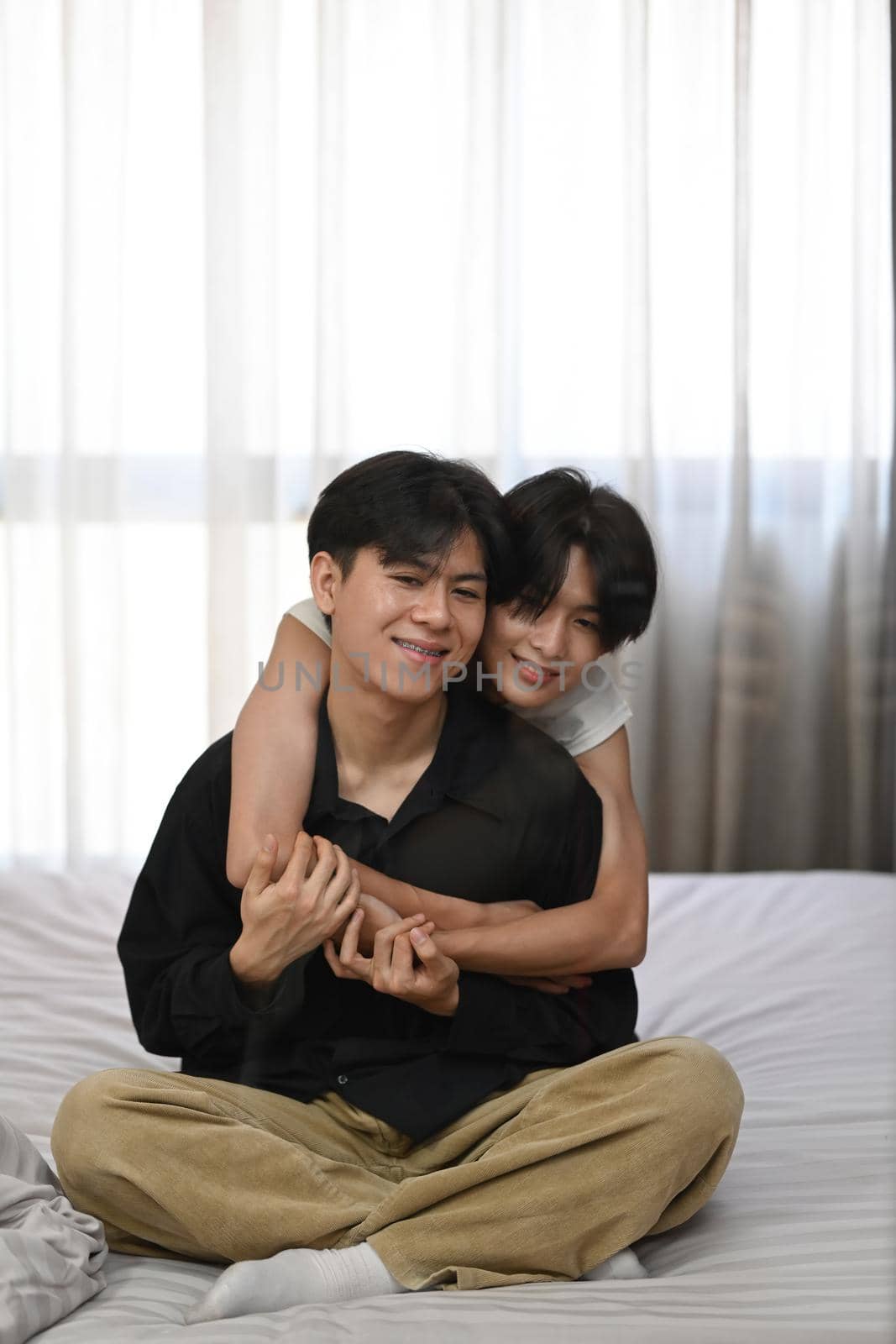Young gay sitting on bed, hugging each other, spending time at home. Homosexual relationships and alternative love lifestyle concept by prathanchorruangsak