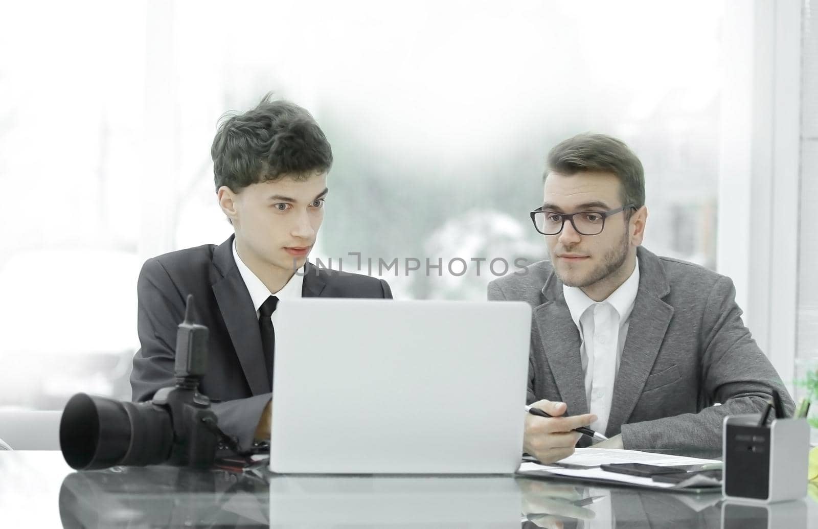 two qualified photographers discuss photos to upload files on a laptop .