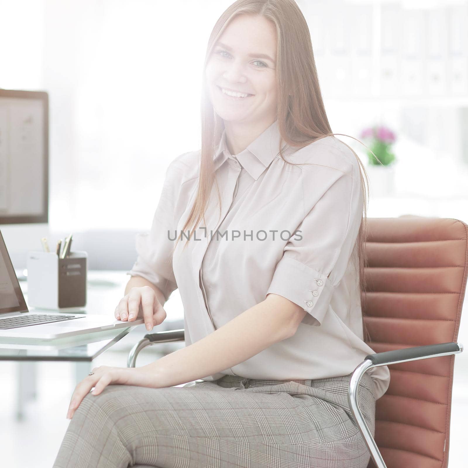 Close-up of young smiling businesswoman sitting at her workplace with laptop near by