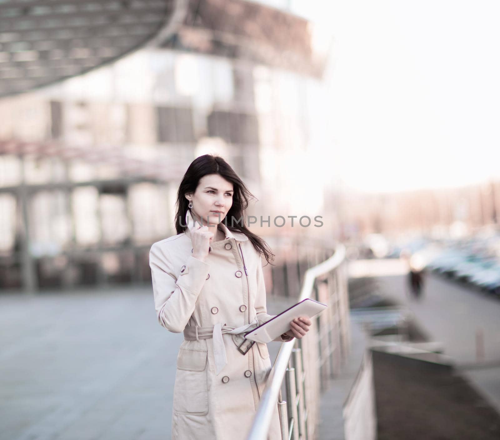 Confident business woman working on a digital tablet, standing next to an office building. The photo has an empty space for your text
