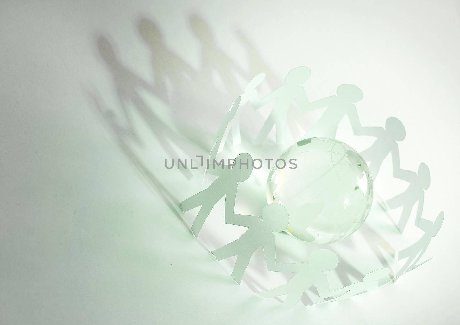 glass globe and a family of paper men on a green background. photo with copy space concept
