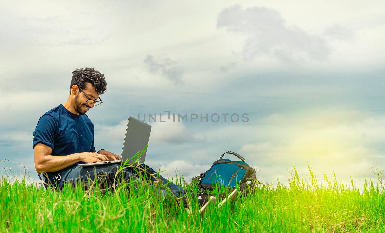 Young man in glasses working on his laptop, man in the field with his computer by isaiphoto