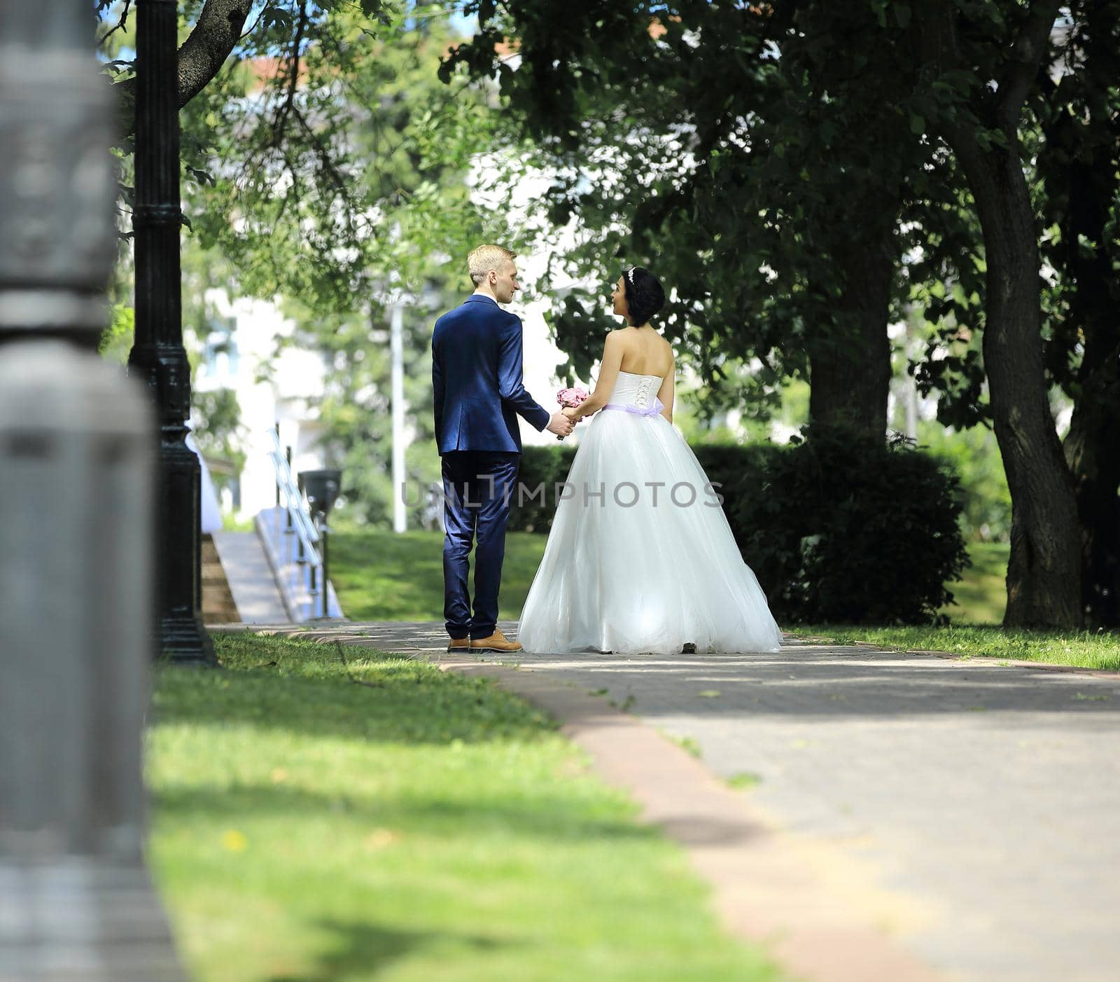 back groom and bride walking along the alley on the background of trees by SmartPhotoLab