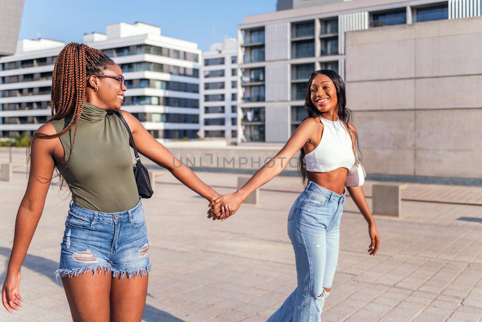 two young african friends walks smiling holding hands, concept of friendship and urban lifestyle