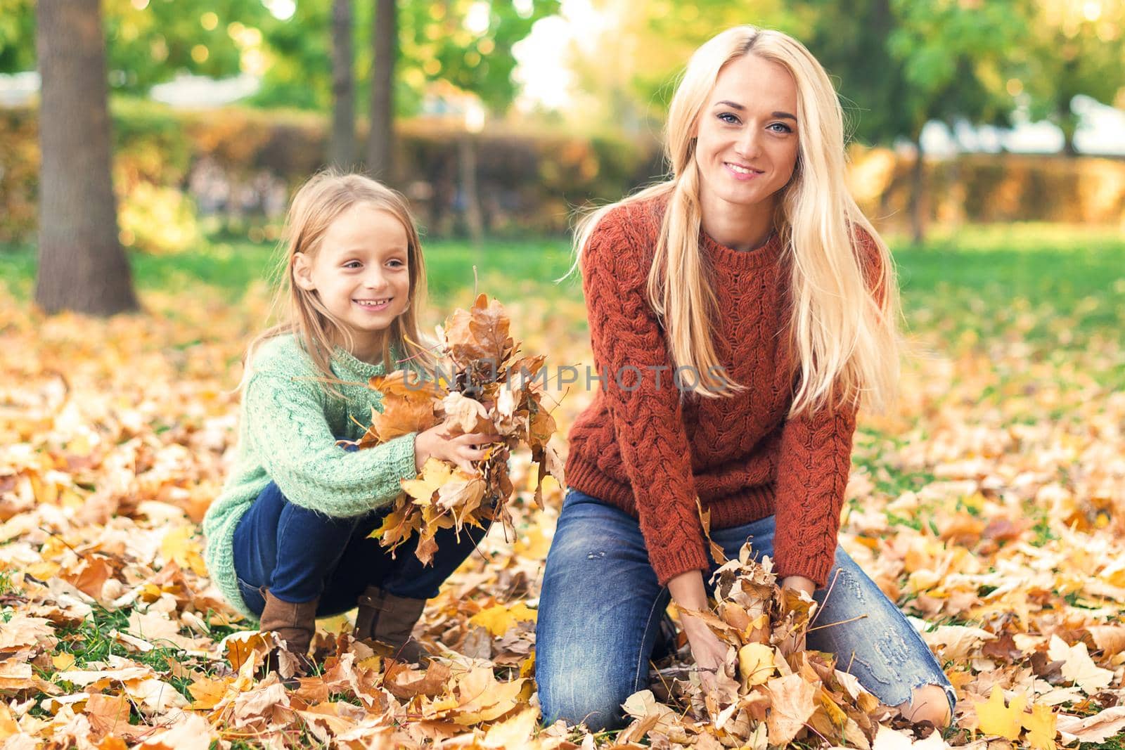 Happy young caucasian mother and little child playing with leaves in nature autumn park