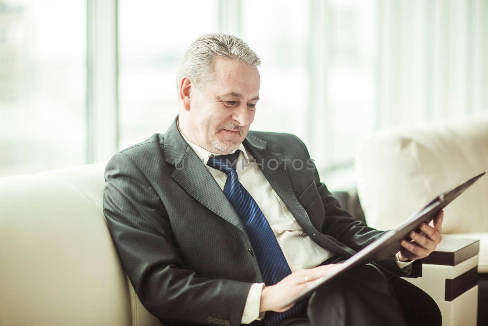 experienced businessman studies working papers sitting on a white sofa in a private office