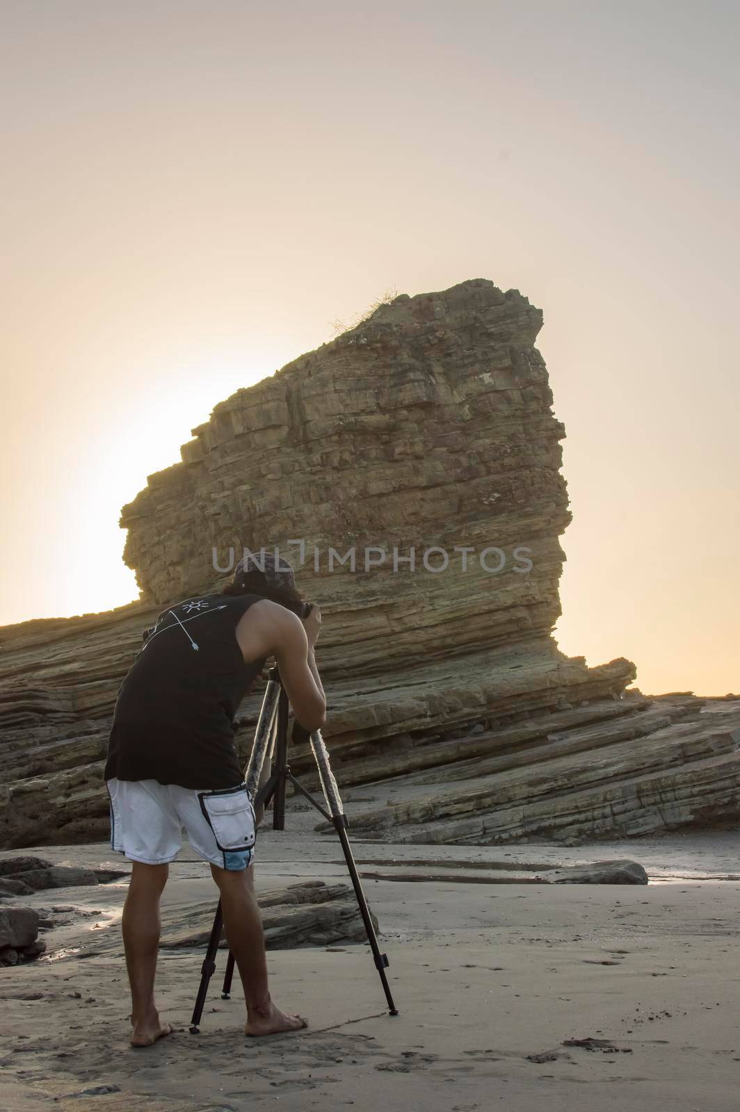 young man taking photo on the beach, man photographing with tripod at sea