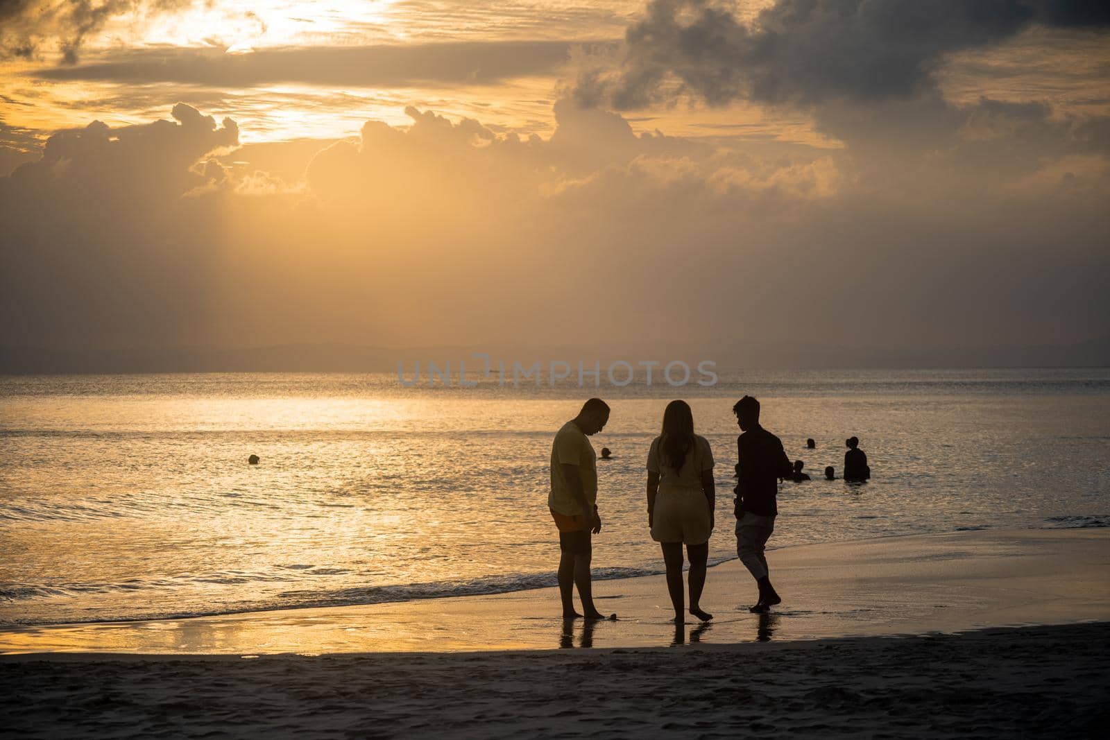 silhouette of of trio of people standing around enjoying during sunset dusk at radhasagar beach with the waves coming on the shore in havelock andaman by Shalinimathur