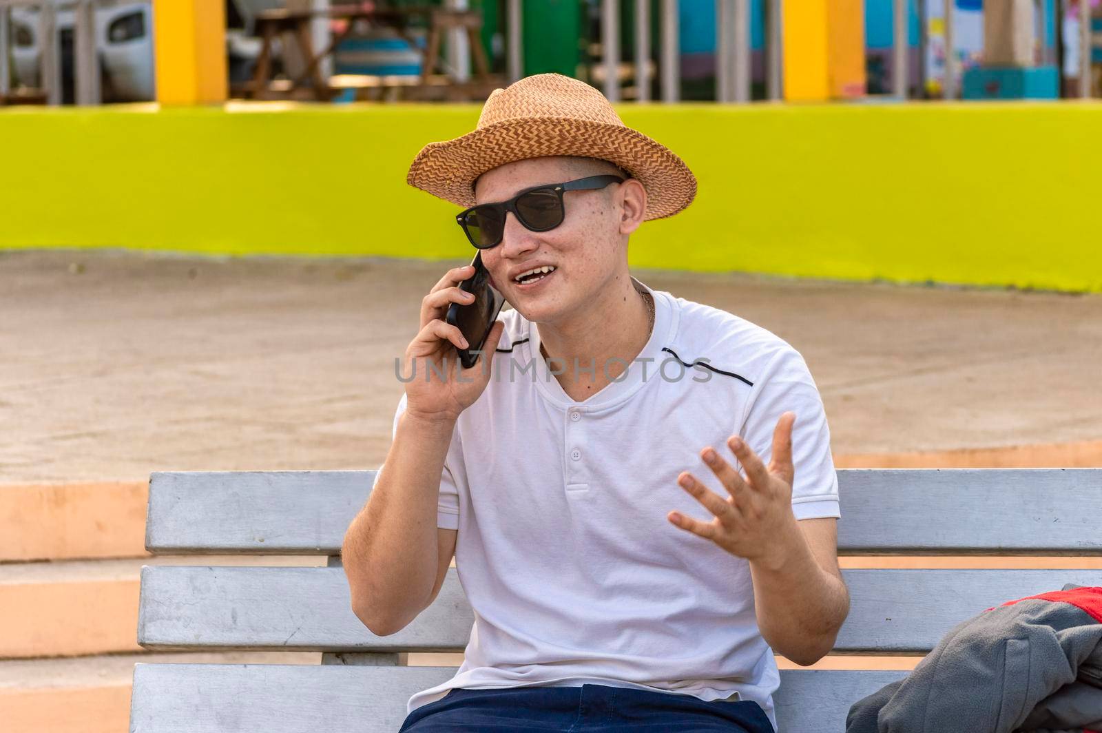 An attractive guy calling on a cell phone on a bench, a man sitting on a bench calling on the phone. by isaiphoto