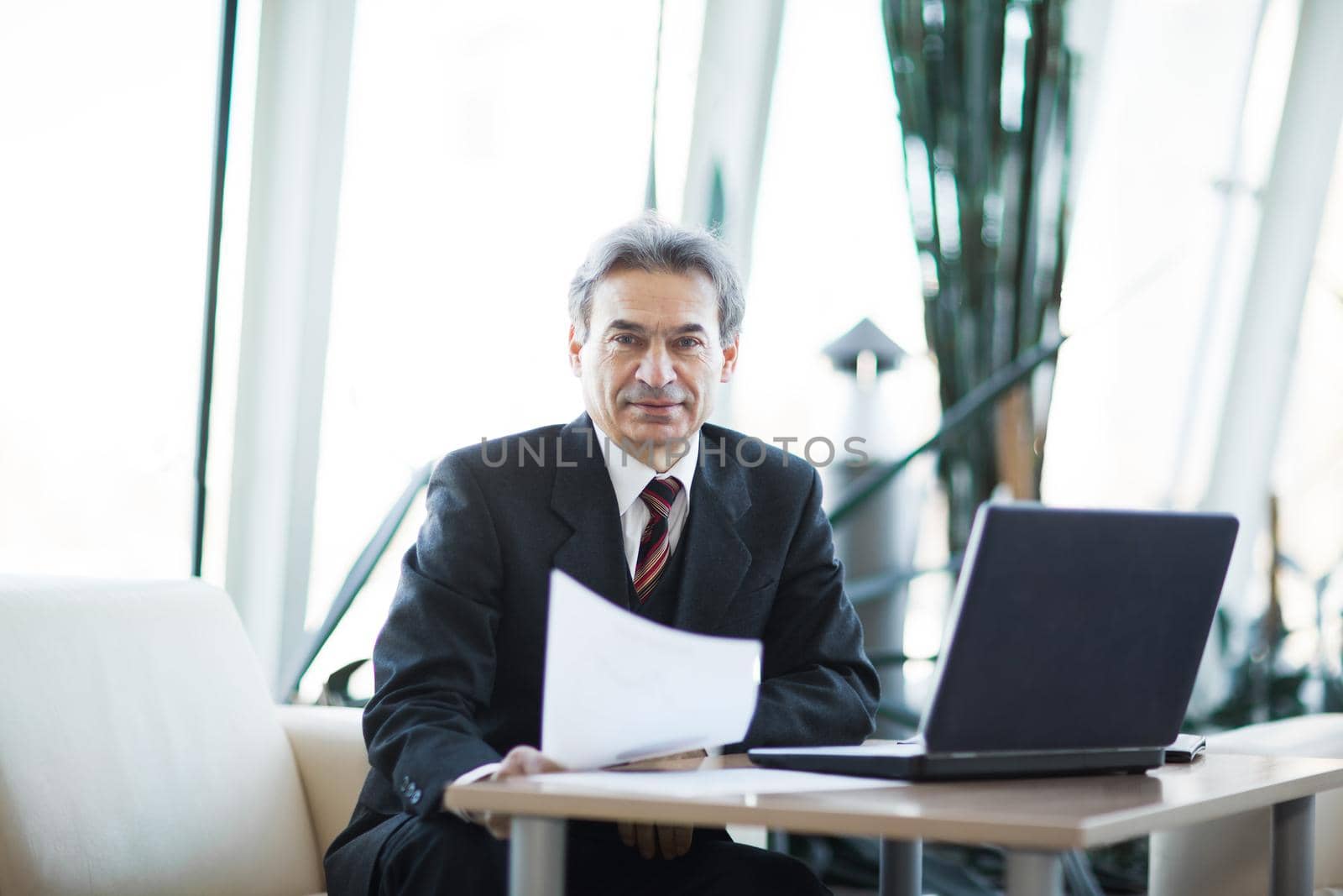 Confident businessman with documents on a laptop in modern office
