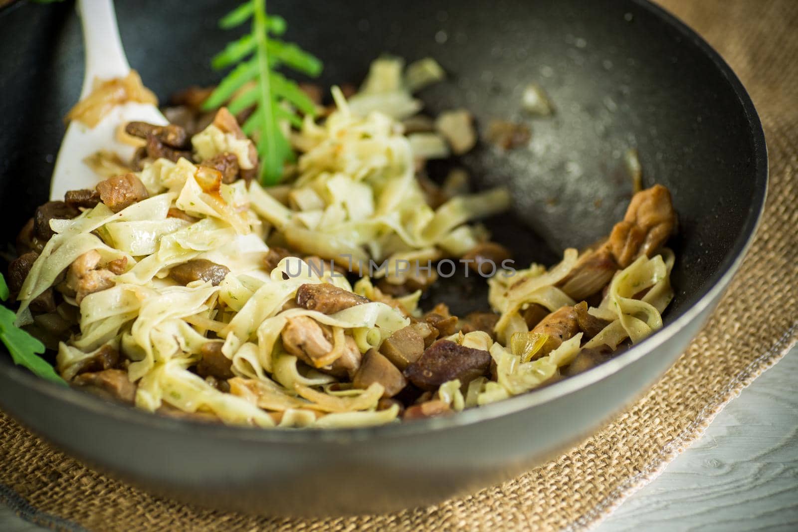 Homemade boiled noodles with meat and eggplant in a frying pan on a wooden table