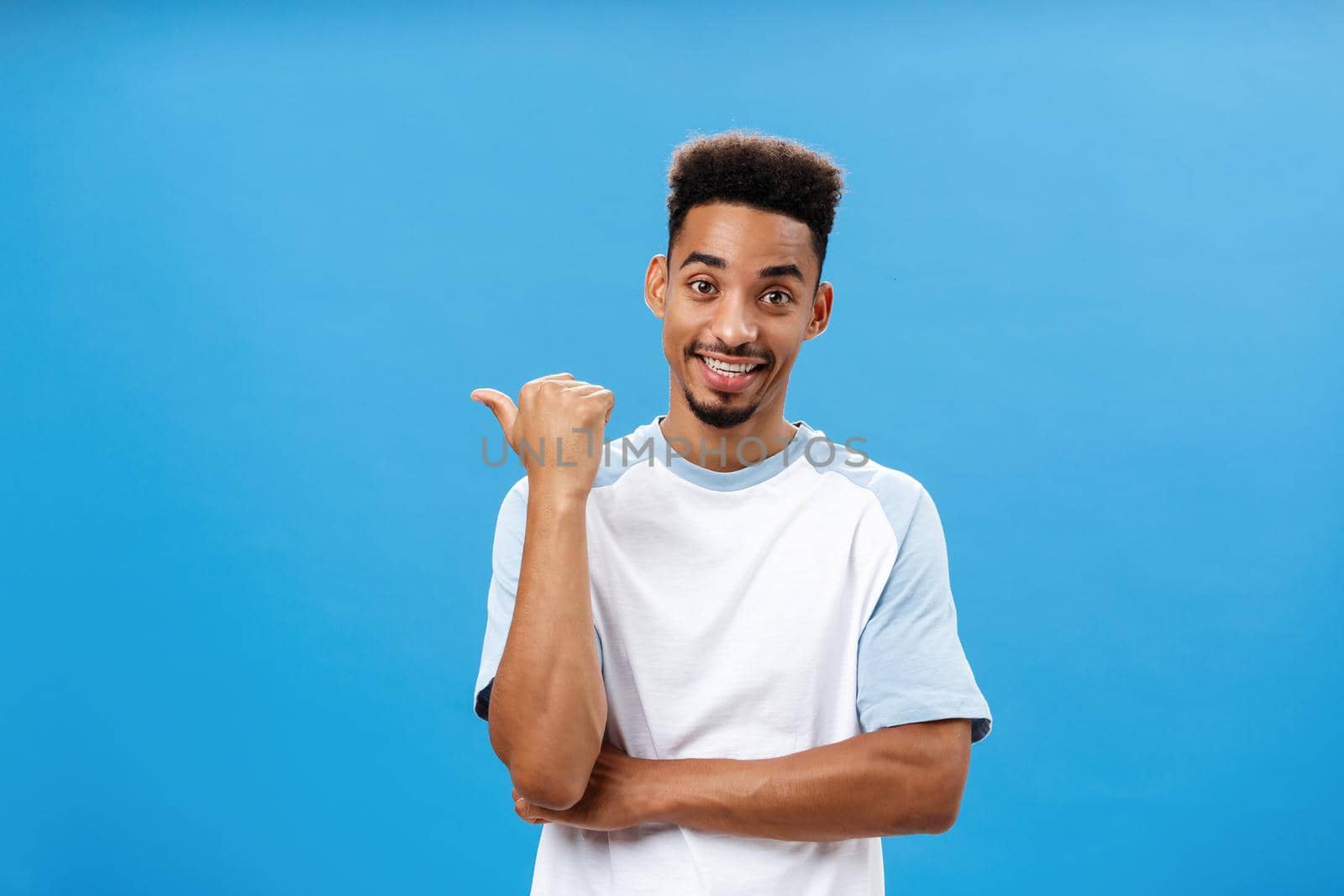 Portrait Lifestyle. Attractive skillful coworker indicating at friend who can solve situation standing relaxed and carefree over blue background pointing left or backwards with thumb and smiling while casually talking.