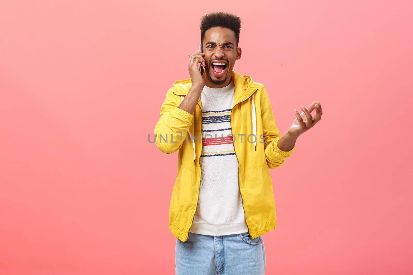 Guy fighting having rough argument with girlfriend via phone call yelling in smartphone gesturing from anger and rage holding device near ear shouting pissed over pink background. Technology and negative emotions concept