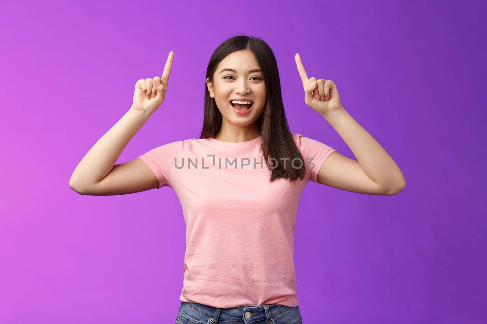 Charismatic good-looking lively smiling asian girl introduce product, pointing fingers up, indicate top advertisement, grinning toothy, excited telling good news, sharing link, purple background by Benzoix