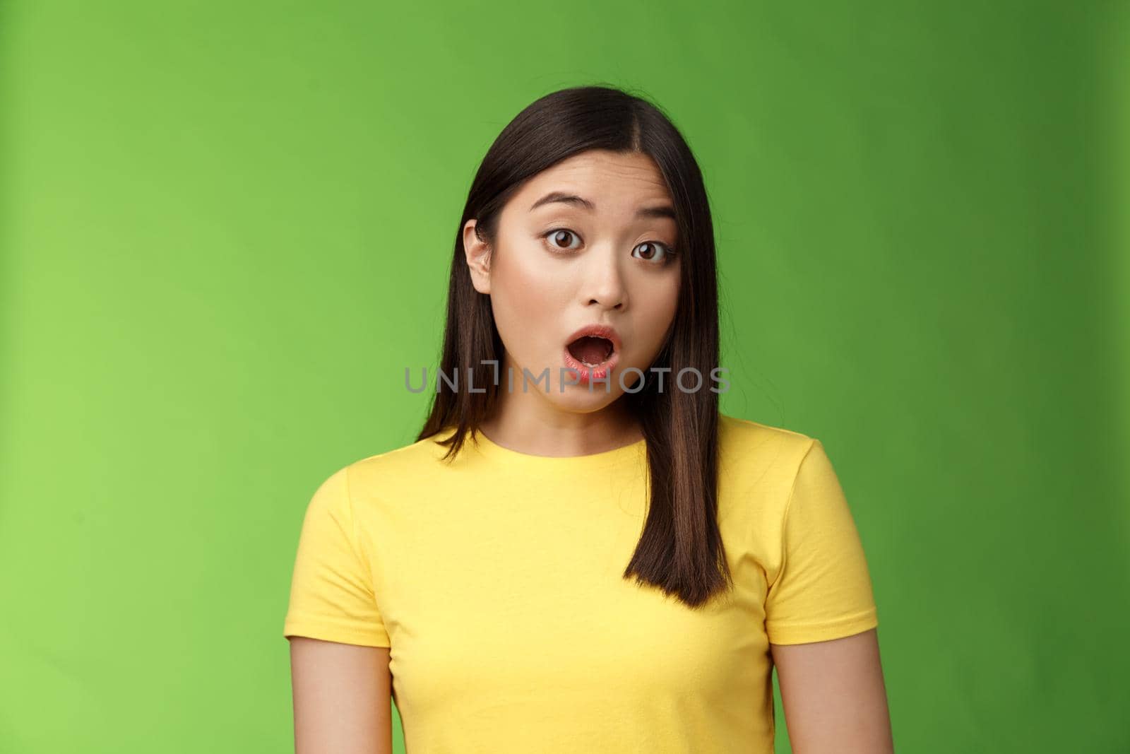 Close-up shocked amazed asian brunette female astonished hear stunning gossip, drop jaw stare camera speechless stand stupor green background, surprised what happening, wear yellow t-shirt by Benzoix