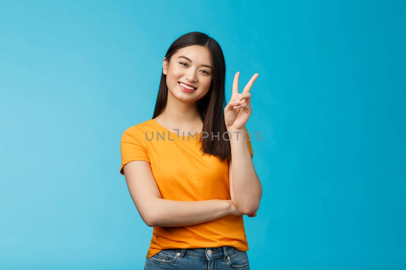 Optimistic cute tender asian young millennial girl send positive vibes, tilt head show peace, victory sign, smiling broadly, wish fantastic holidays, stand blue background joyful upbeat.