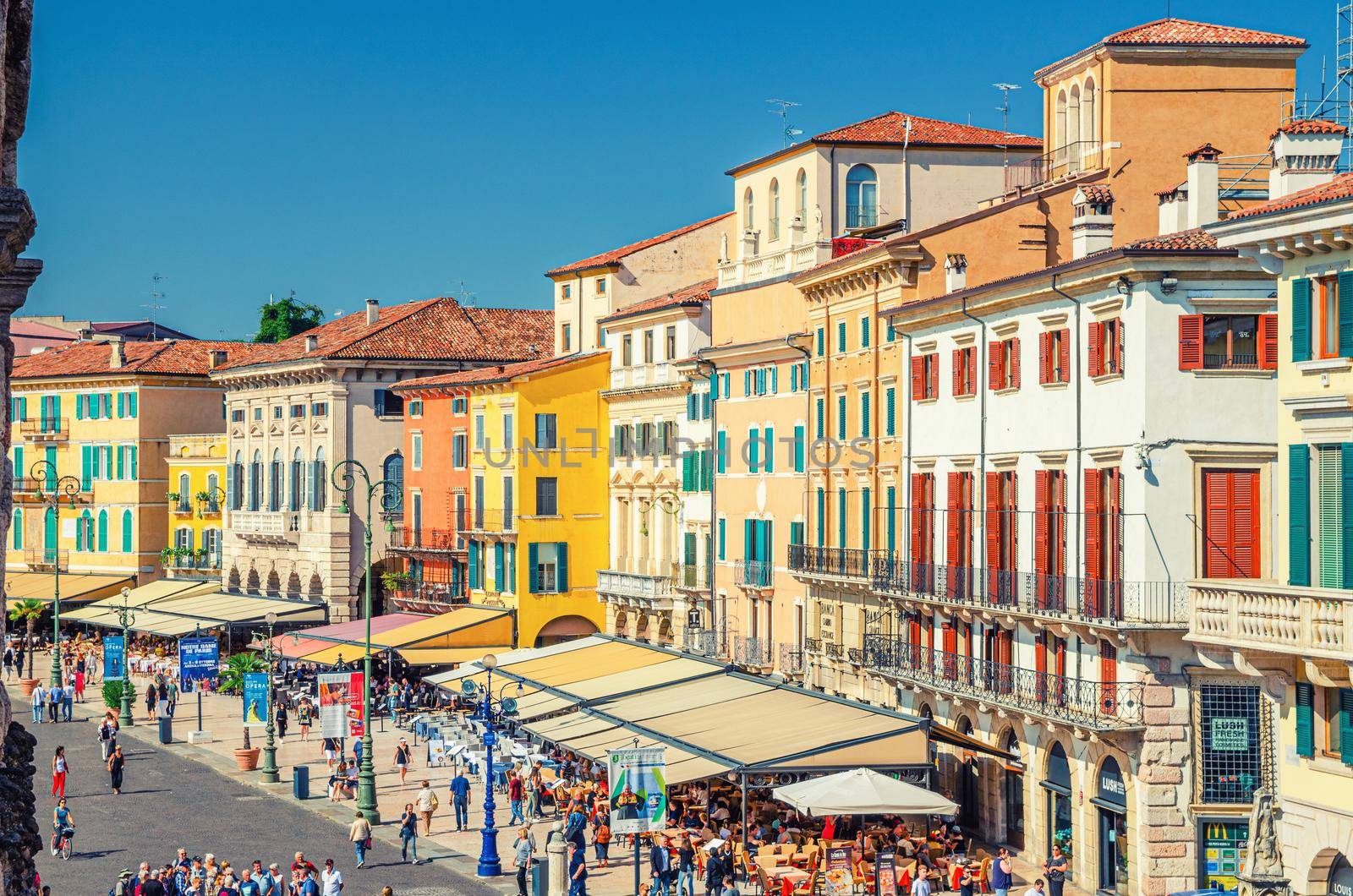 Verona, Italy, September 12, 2019: Row of old colorful multicolored buildings on Piazza Bra square in historical city centre, cafes and restaurants with tents and walking tourists, aerial view