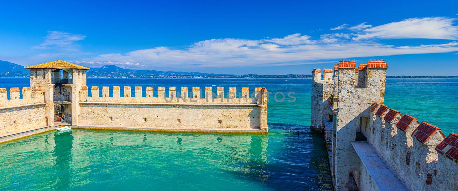Sirmione, Italy, September 11, 2019: Small fortified harbor with turquoise water, Scaligero Castle Castello fortress, town on Garda lake, medieval castle with stone towers and brick walls, Lombardy
