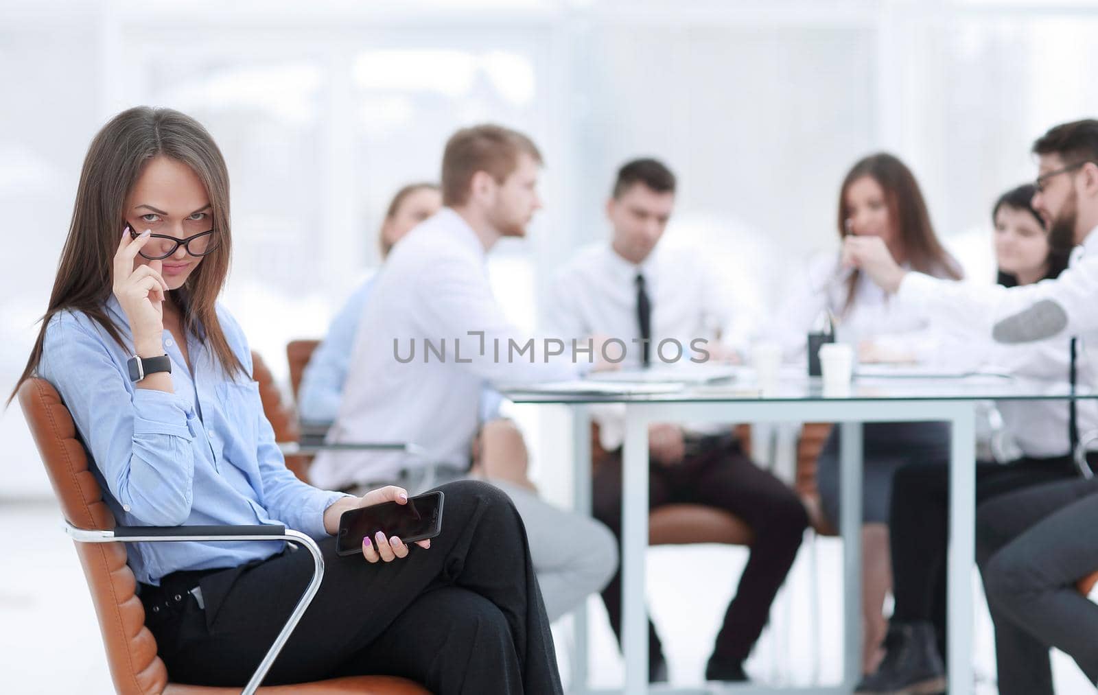 Executive businesswoman with smartphone on blurred background of business team.