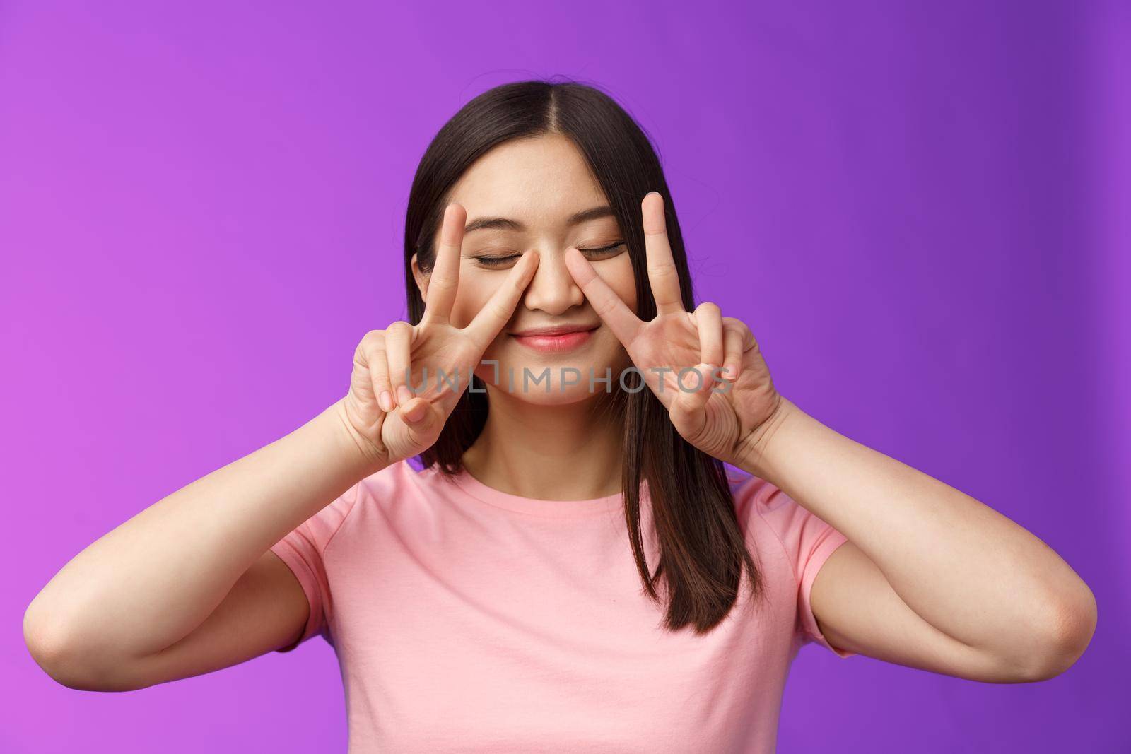 Close-up carefree friendly cute tender asian woman feeling upbeat, close eyes and smiling dreamy, show victory peace signs on face, stay positive, enjoy summer holiday, stand purple background.