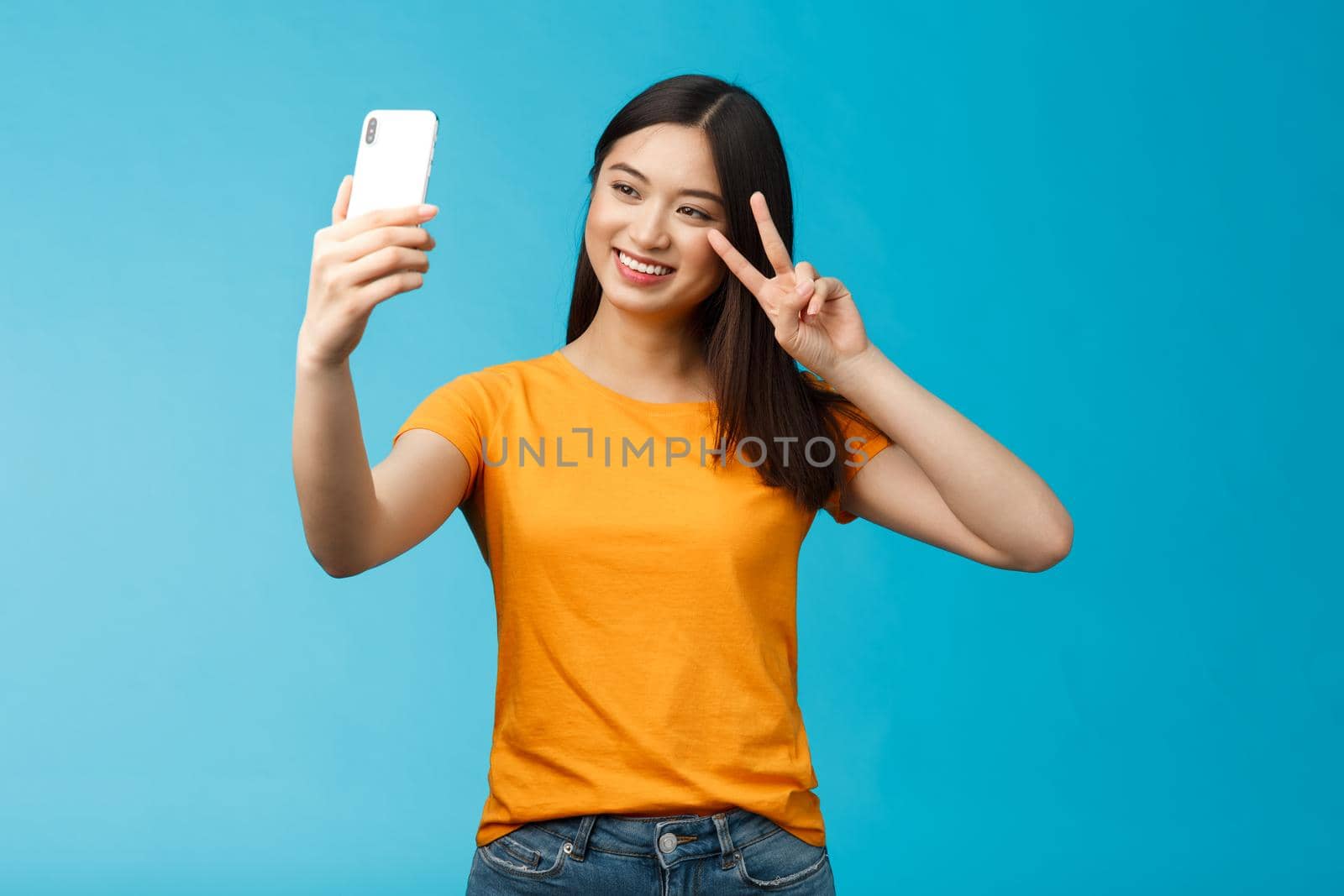 Friendly cheerful pretty asian woman brunette short haircut taking selfie, smiling joyfully hold smartphone show peace, victory sign at phone screen front camera, talking family video-call.