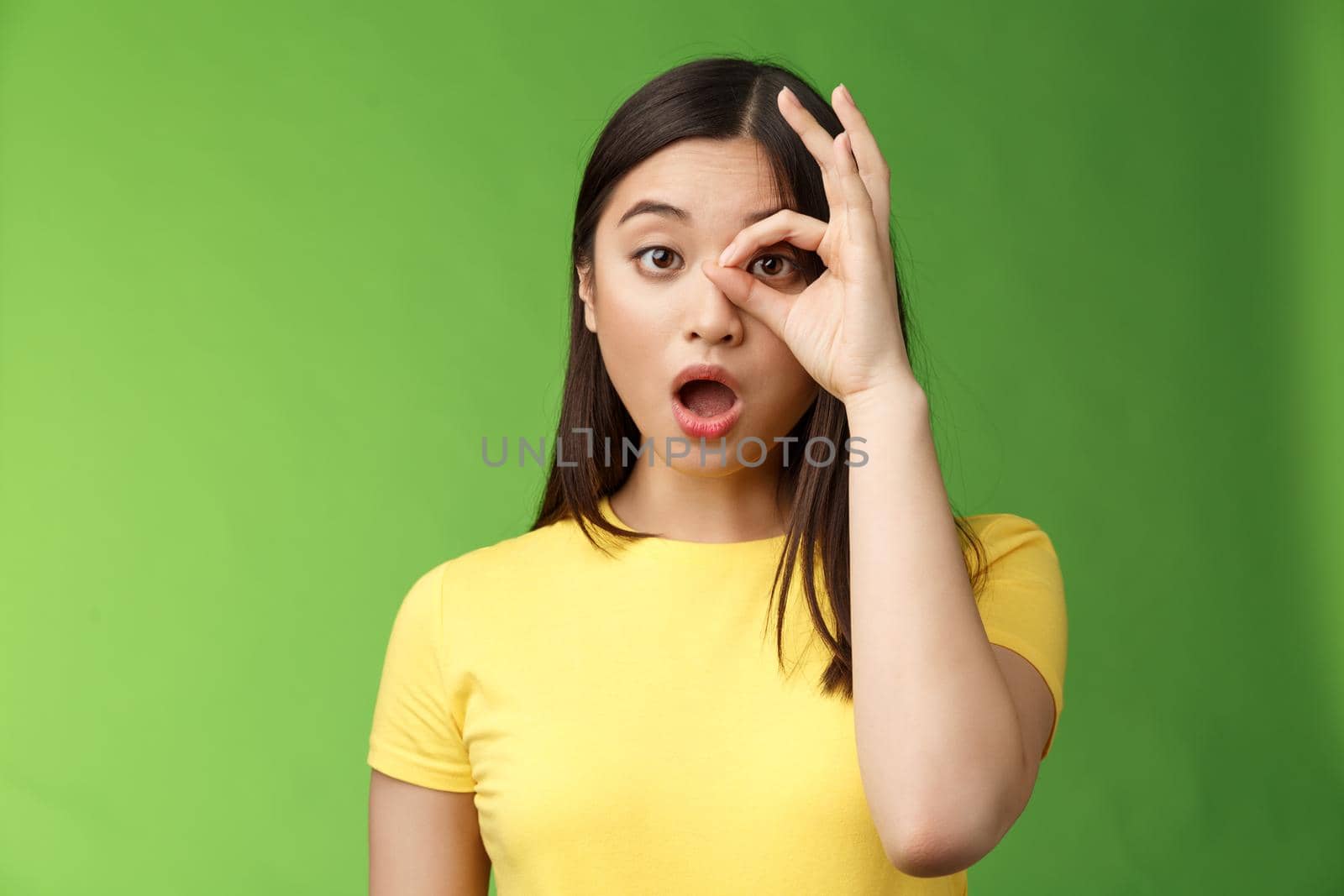 Amazed speechless cute asian young girl drop jaw astonished, look through ok circle sign, drop jaw speechless, impressed look camera, check out incredible promo, stand green background by Benzoix